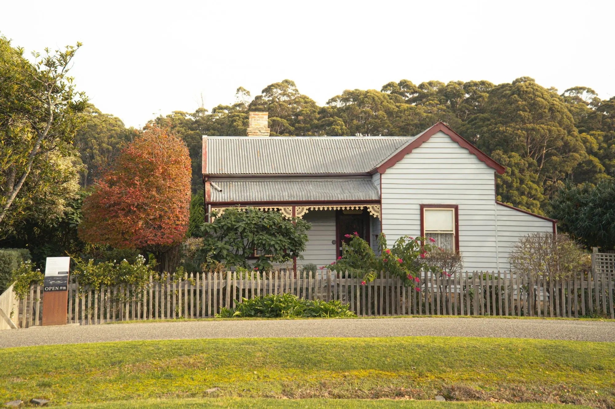 Weatherboard cottage with a corrugated iron roof, picket fence and autumn garden in Port Arthur, Tasmania